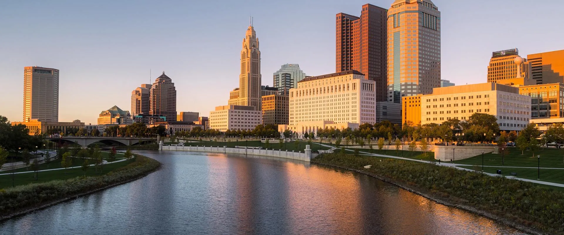 Cleveland, Ohio skyline with modern buildings and a river flowing through the cityscape under a clear blue sky.