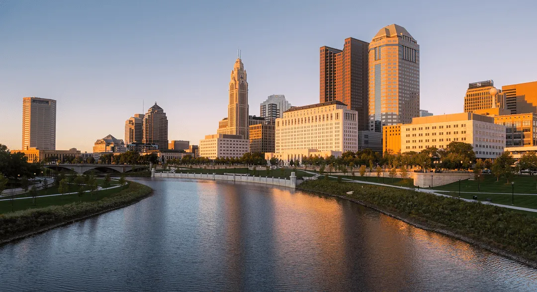 Cleveland, Ohio skyline with modern buildings and a river flowing through the cityscape under a clear blue sky.